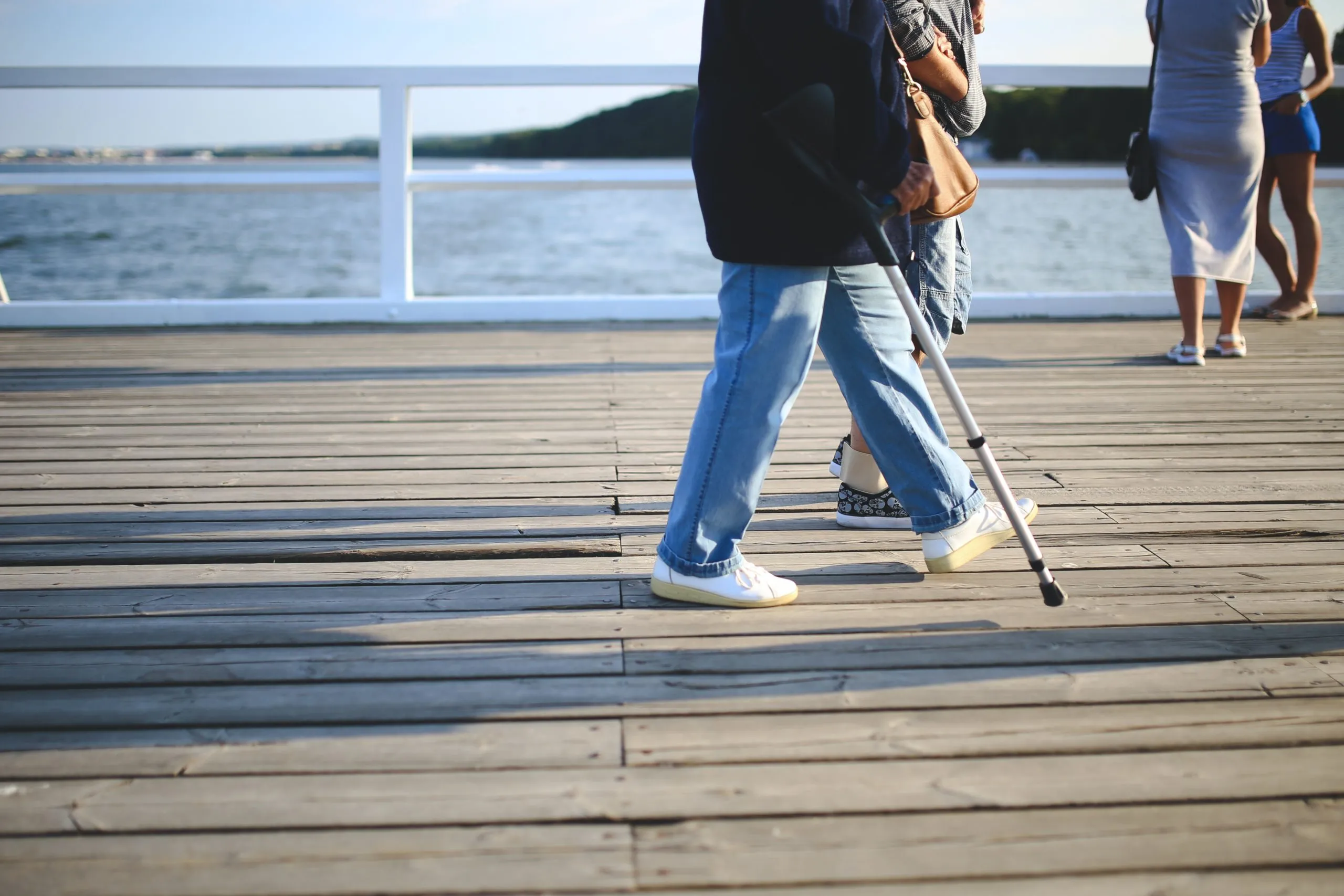 Photo of someone with a crutch walking along a peer with someone else