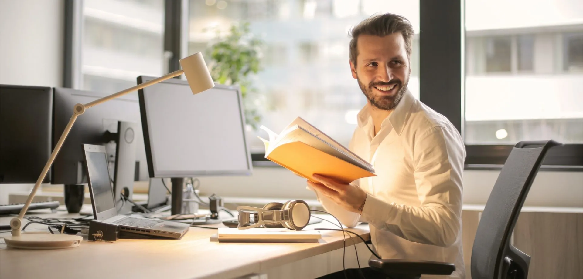 man sat at office desk smiling with journal in hand