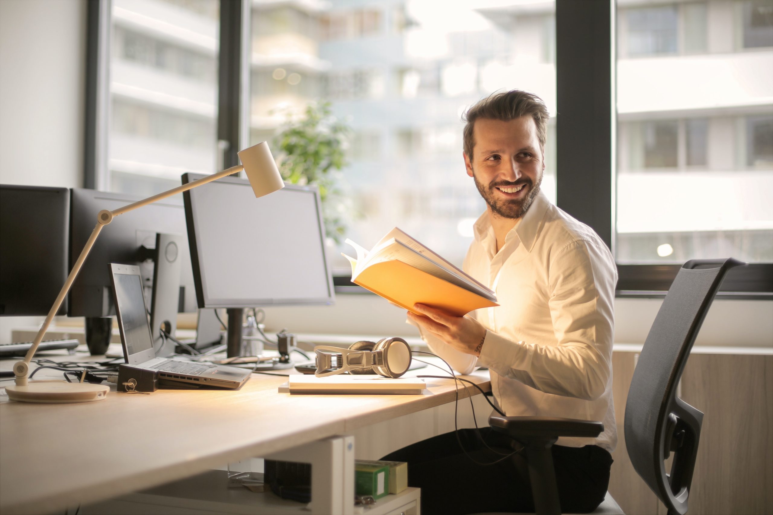 man sat at office desk smiling with journal in hand